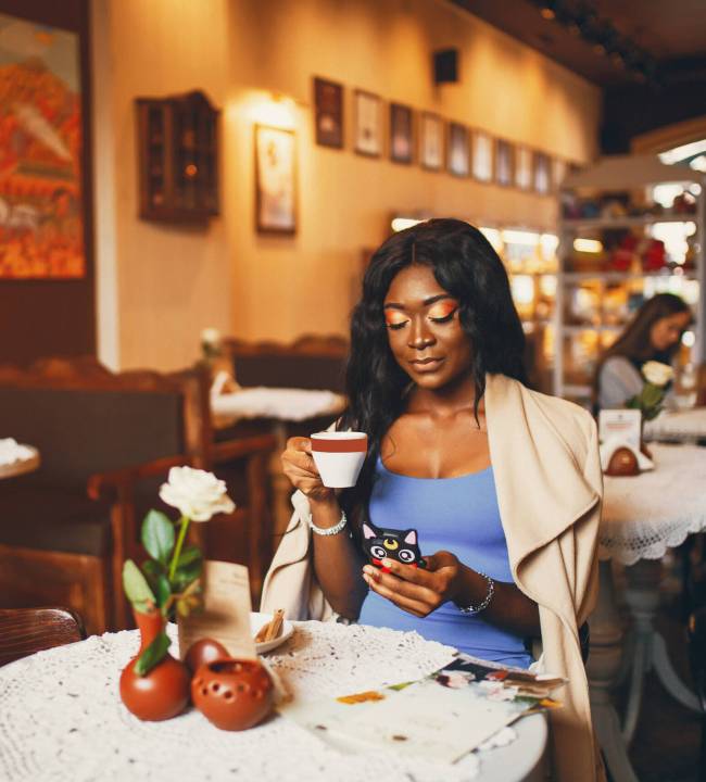 Elegant black woman sitting in a cafe. Businesswoman drinking a coffee. Woman use the phone