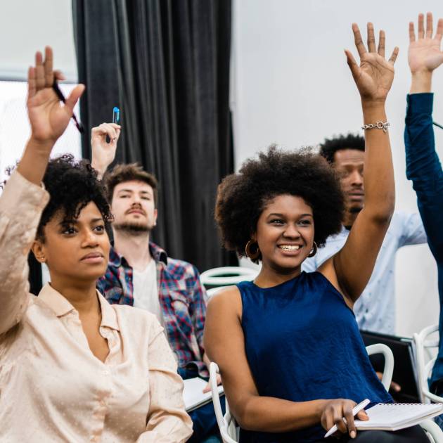 Group of young people sitting on conference together while raising their hands to ask a question. Business team meeting seminar training concept.